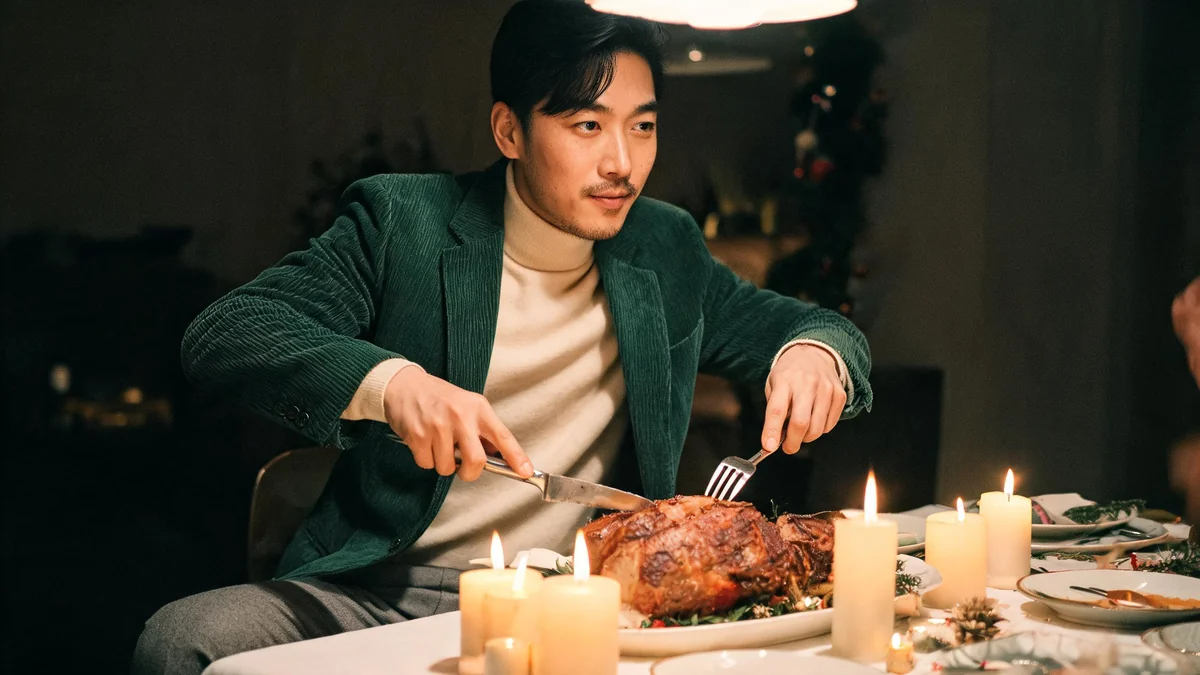 Man in his late thirties in a bottle-green corduroy blazer, cream merino rollneck and grey wool trousers at a dinner table set for Christmas