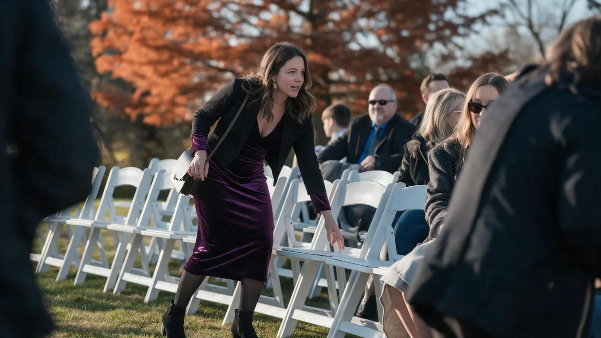 Guest in a long-sleeve plum midi dress with black tights, heeled ankle boots and a cropped blazer at an outdoor autumn ceremony