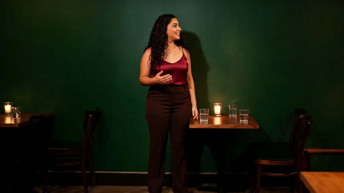 Woman at a candlelit restaurant table in a burgundy silk camisole and dark brown high-waisted trousers