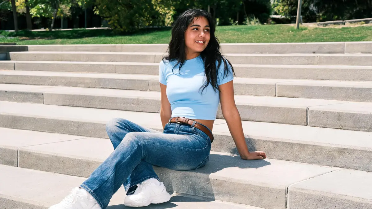 Young woman in low-rise medium-wash flared jeans, a fitted baby blue baby tee and chunky white sneakers