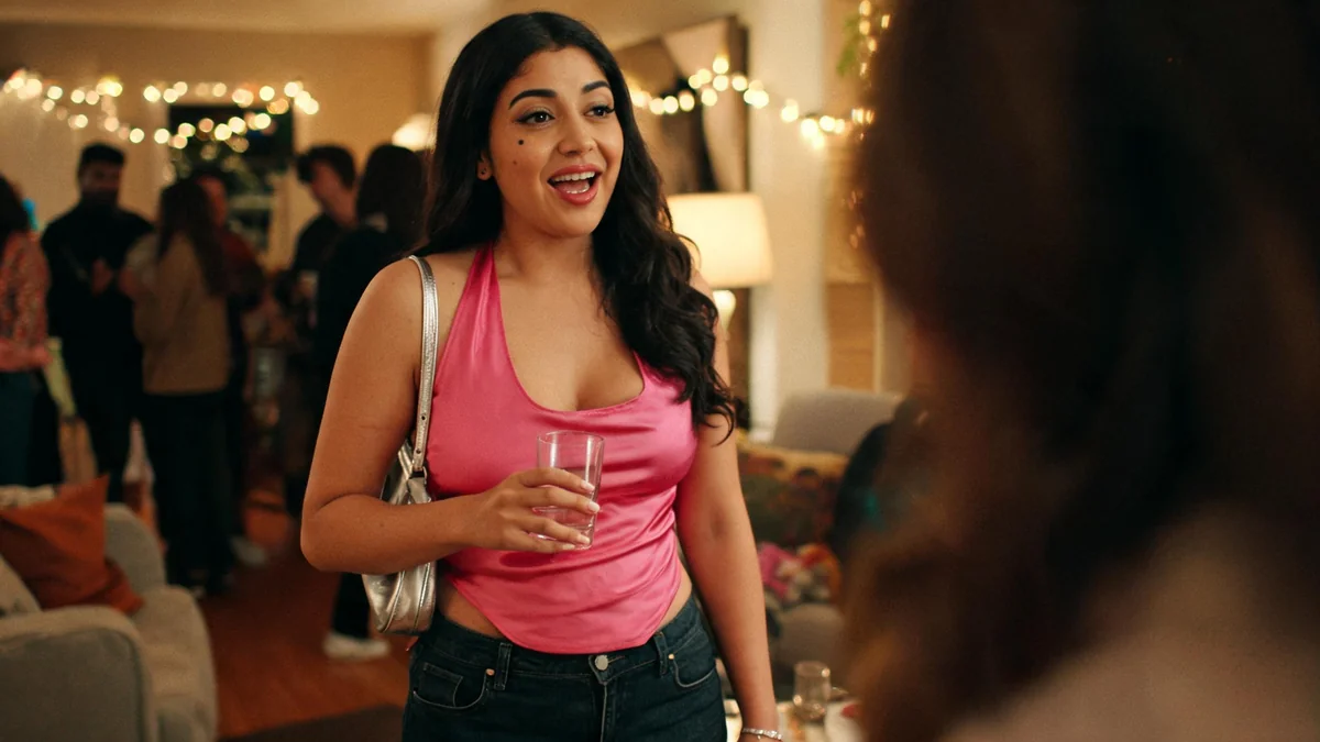 Woman in a hot pink satin halter top, dark flared jeans and strappy heeled sandals at a house party